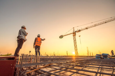 Shutterstock. Bouwkundig ingenieurs die toezicht houden op de voortgang van het bouwproject staan op een nieuwe betonnen vloer op het dak met een kraan op de achtergrond.